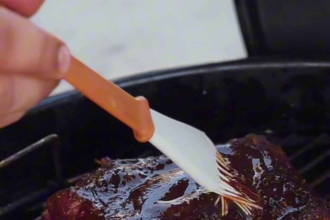 Стейк на гриле смазывают BBQ-соусом кистью