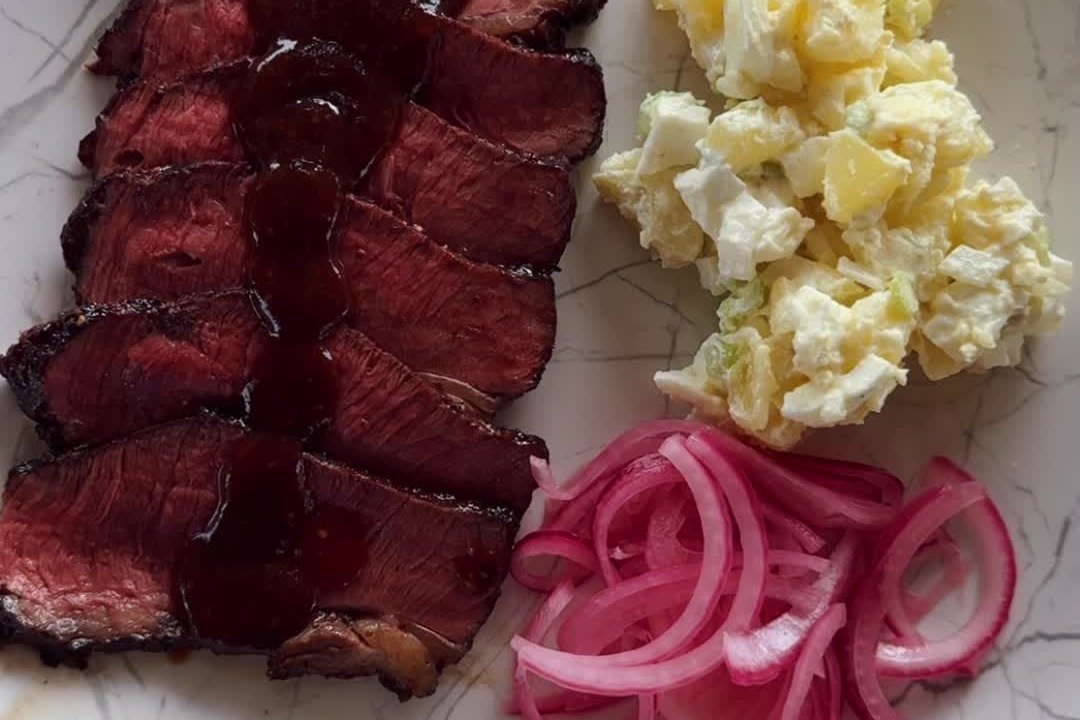 Слайсы стейка в BBQ-глазури, картофельный салат и маринованный красный лук на тарелке
