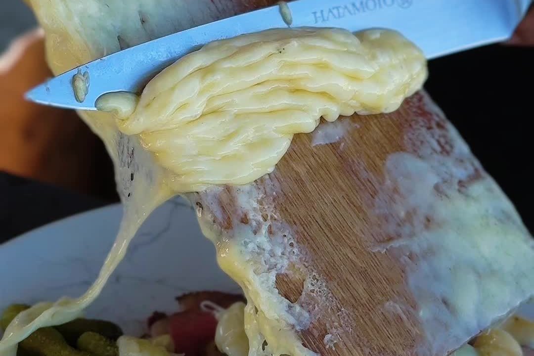 Расплавленный сыр снимают ножом с дощечки на мясо с картофелем